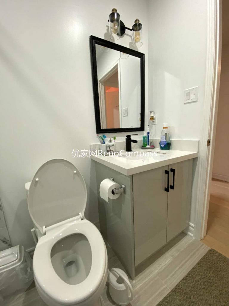 This image showcases a completed bathroom renovation project in Mississauga, featuring a clean and functional vanity layout with integrated storage, a modern toilet installation, and a framed mirror with wall-mounted lighting. Neutral color cabinetry and durable countertop materials enhance both practicality and visual balance, making the space easy to maintain for long-term daily use. The compact layout maximizes efficiency while maintaining a bright, modern appearance, reflecting the attention to detail and craftsmanship expected from a professional Toronto renovation company.