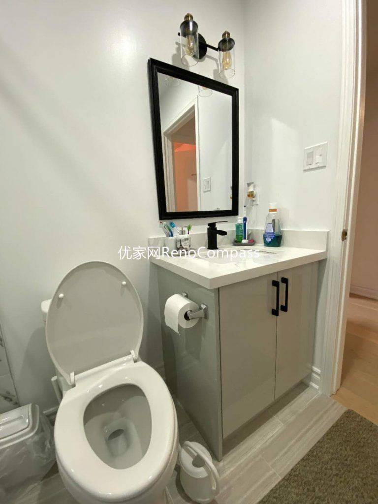 This image showcases a completed bathroom renovation project in Mississauga, featuring a clean and functional vanity layout with integrated storage, a modern toilet installation, and a framed mirror with wall-mounted lighting. Neutral color cabinetry and durable countertop materials enhance both practicality and visual balance, making the space easy to maintain for long-term daily use. The compact layout maximizes efficiency while maintaining a bright, modern appearance, reflecting the attention to detail and craftsmanship expected from a professional Toronto renovation company.