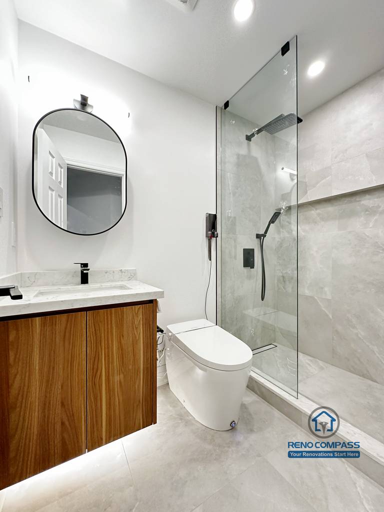 Bathroom renovation in Markham featuring a custom wood vanity with quartz countertop, vessel sink, brass fixtures, and a rounded backlit mirror. Vertical wood paneling and minimalist finishes create a warm, modern powder room with clean proportions and refined detailing.