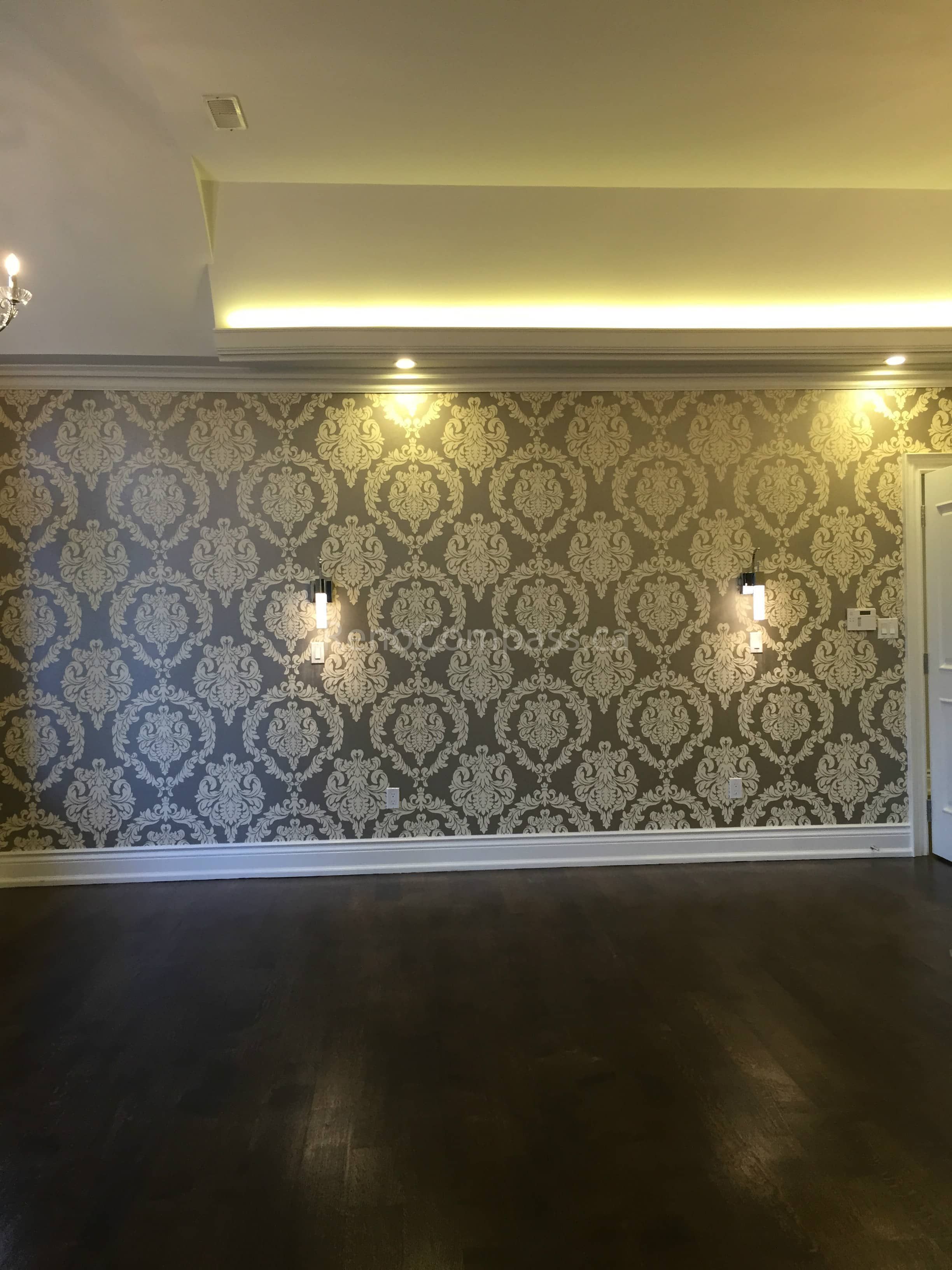 This Toronto interior renovation showcases a sophisticated feature wall with classic patterned wallpaper, decorative wall sconces, and a recessed LED ceiling lighting system. The rich hardwood flooring and crown molding details enhance the overall elegance, creating a warm and luxurious living space. Completed by Reno Compass Inc., a professional Toronto renovation company specializing in high-end interior remodeling and custom home upgrades.