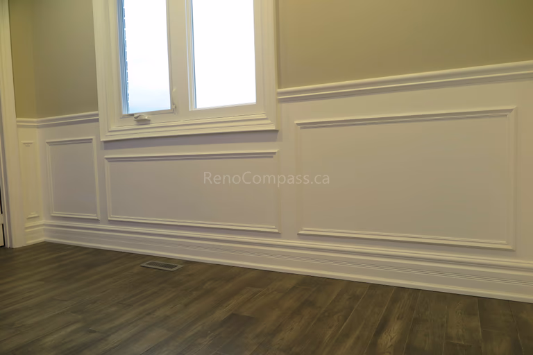 This Markham interior renovation showcases a bright and elegant living space featuring custom wall panel molding, crown molding details, and newly installed dark hardwood flooring. Recessed LED pot lights provide balanced lighting throughout the room, while large windows enhance natural light and openness. Completed by Reno Compass, a professional renovation contractor specializing in high-quality interior renovations and custom finishing services across Markham and the Greater Toronto Area.