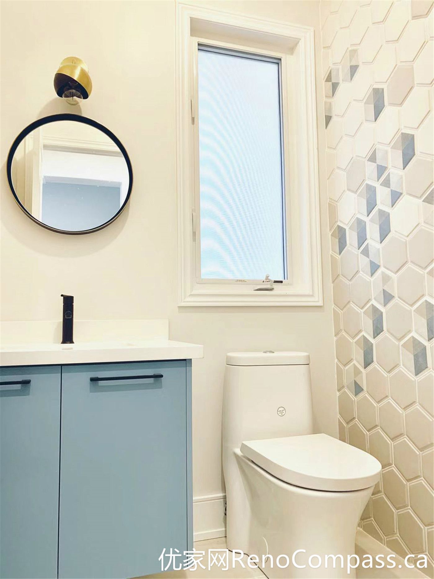 This Markham home renovation highlights a stylish bathroom featuring a soft blue vanity, round mirror, and a decorative hexagon tile accent wall. The combination of warm lighting, modern fixtures, and natural daylight from the window creates a cozy yet contemporary atmosphere with strong visual character.