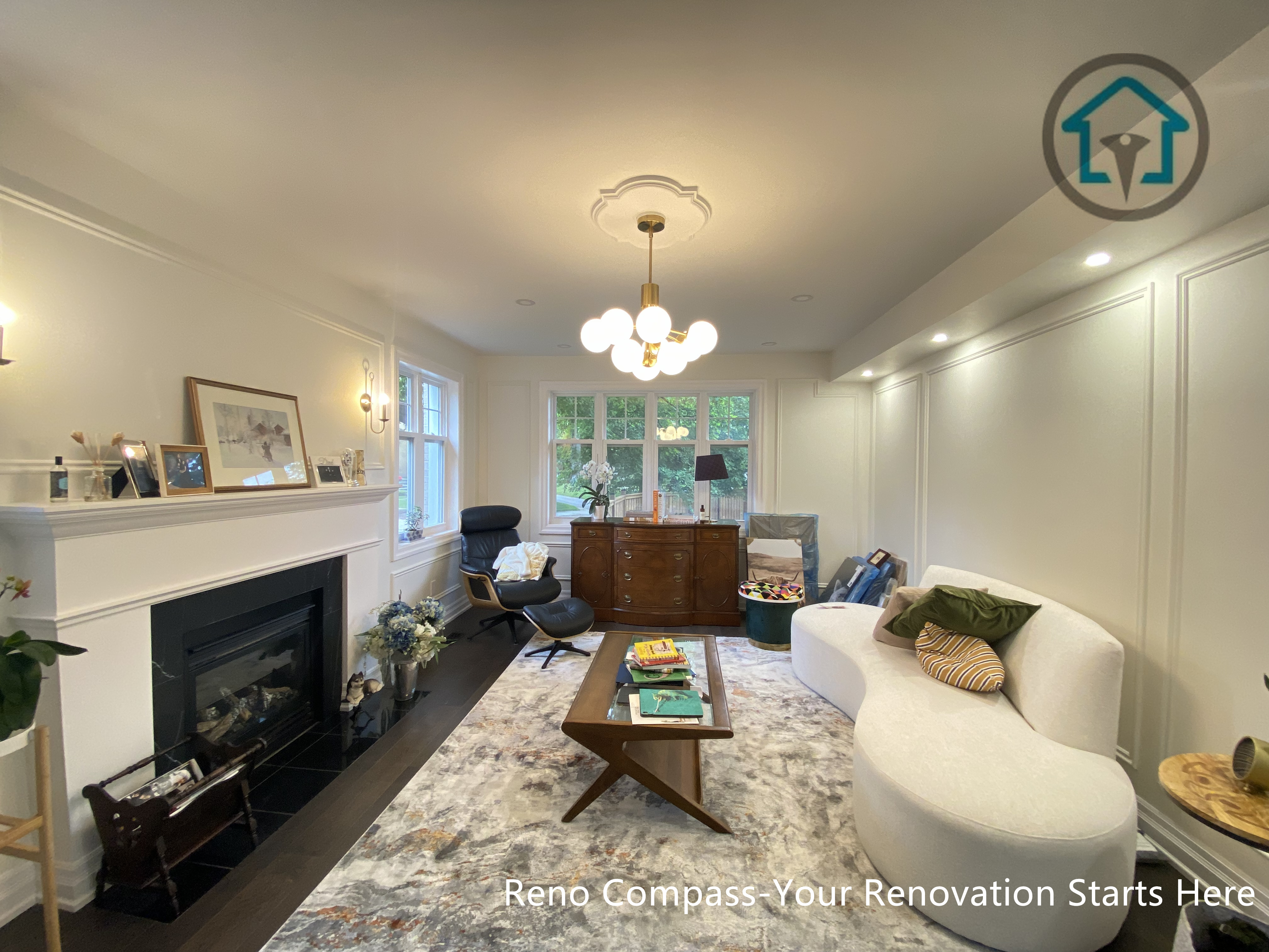 This Toronto living room renovation highlights a balanced and symmetrical layout centered around a classic fireplace feature. Wall paneling, ceiling detailing, and coordinated lighting fixtures establish a calm and cohesive visual rhythm throughout the space. Large rear-facing windows introduce natural light while maintaining privacy, and the furniture arrangement supports both relaxation and conversation. Neutral tones and layered textures create a welcoming atmosphere suited for everyday living within a thoughtfully renovated Toronto home.