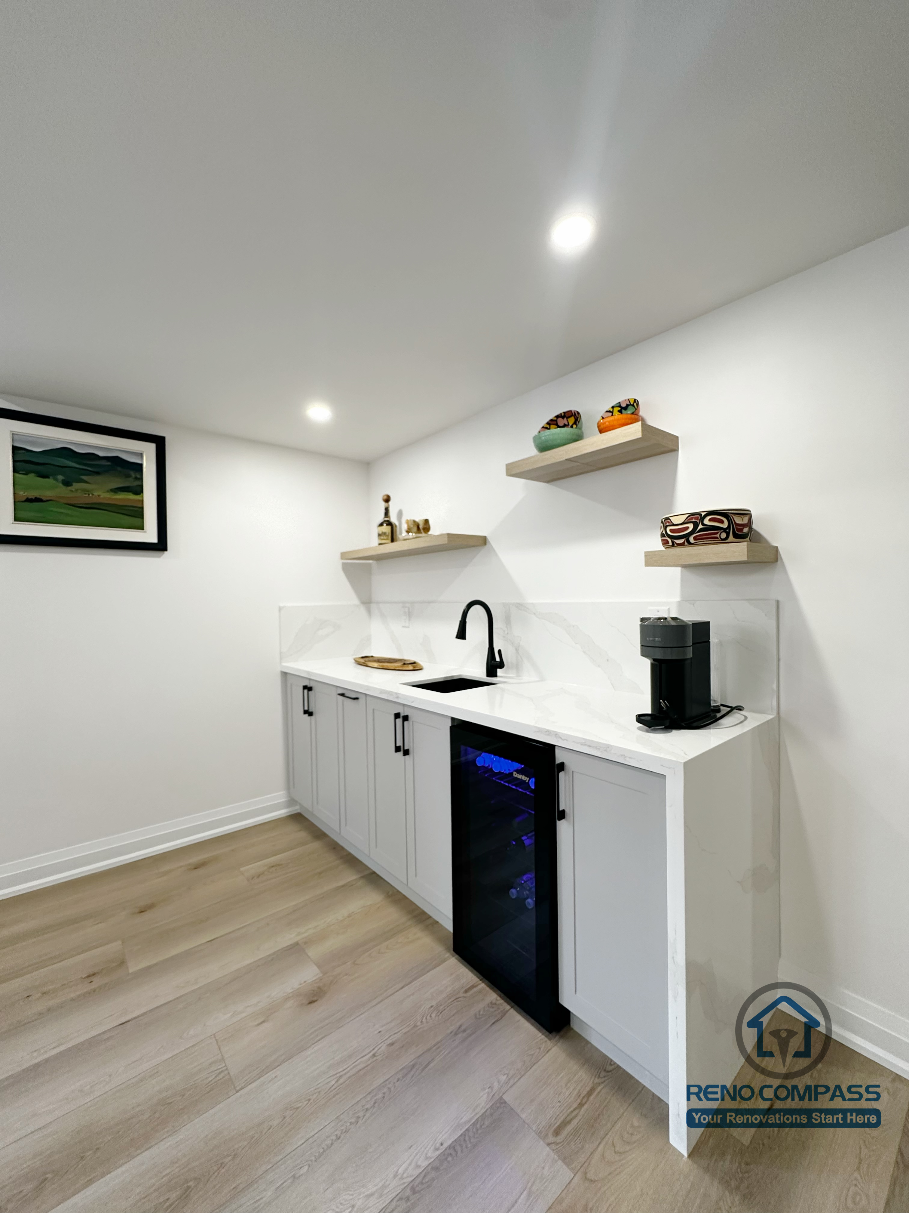 This Richmond Hill basement renovation includes a compact wet bar designed for everyday convenience and entertaining. The space features custom light-grey cabinetry, a clean white countertop, open wood shelving, and integrated under-counter beverage refrigeration. Recessed ceiling lighting and wide-plank flooring keep the area bright and cohesive with the rest of the basement. This wet bar adds both functionality and lifestyle value, making the basement ideal for hosting guests or casual family use.