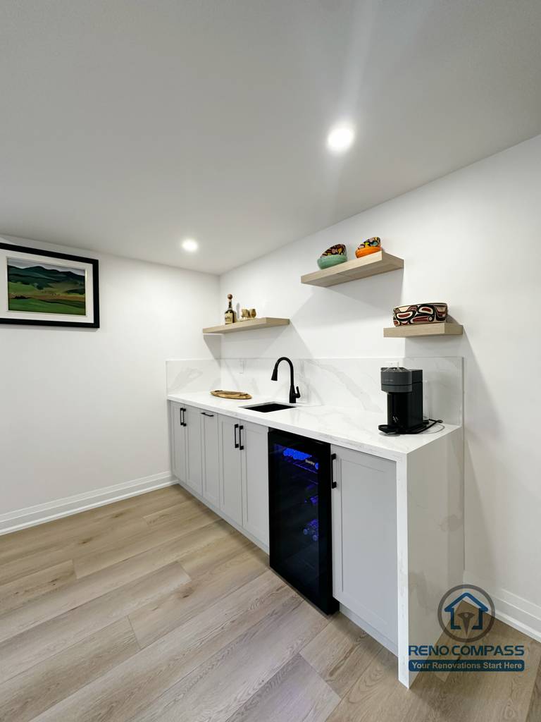 This Richmond Hill basement renovation includes a compact wet bar designed for everyday convenience and entertaining. The space features custom light-grey cabinetry, a clean white countertop, open wood shelving, and integrated under-counter beverage refrigeration. Recessed ceiling lighting and wide-plank flooring keep the area bright and cohesive with the rest of the basement. This wet bar adds both functionality and lifestyle value, making the basement ideal for hosting guests or casual family use.