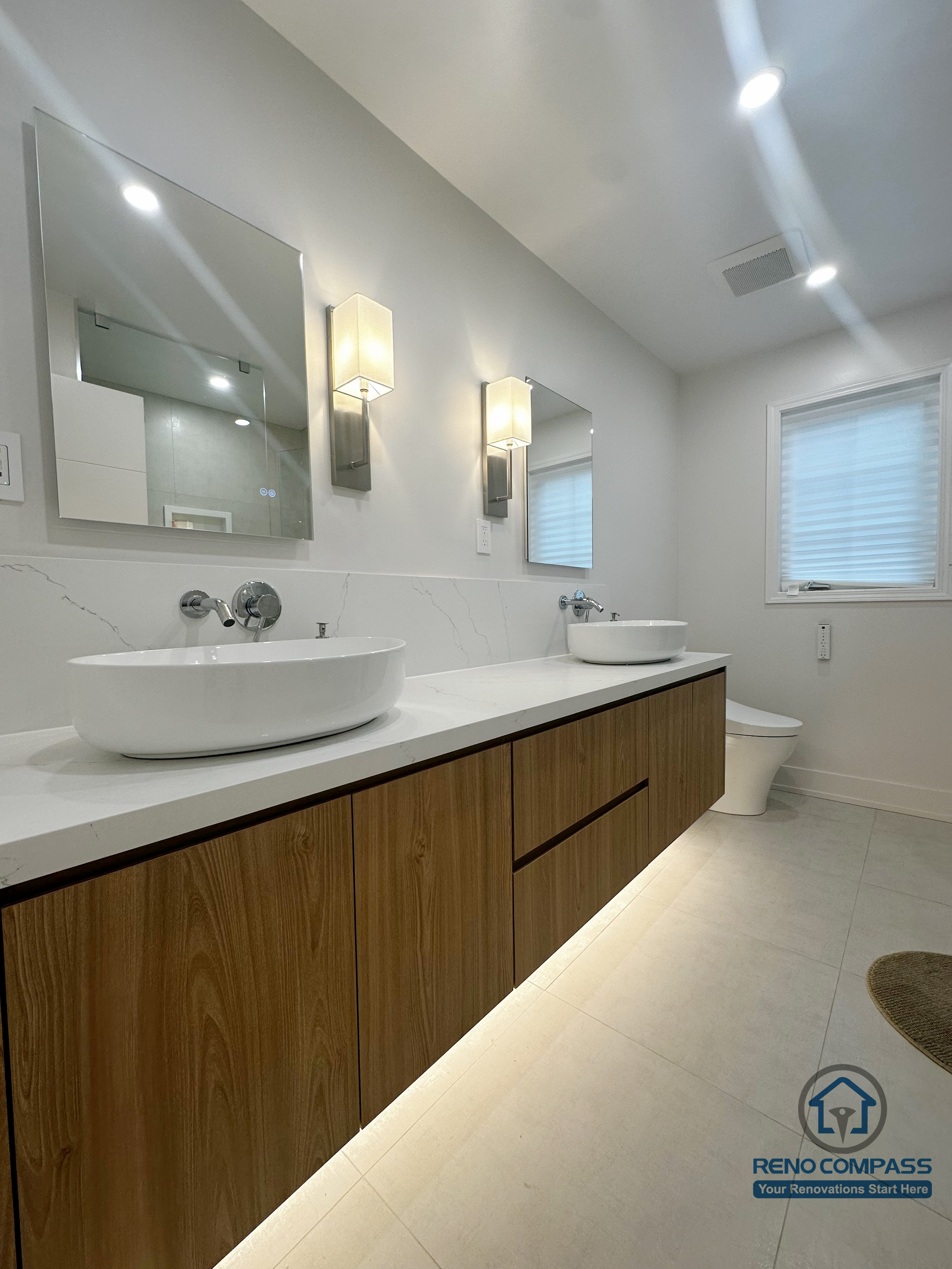 This Oakville bathroom renovation showcases a sleek floating wood vanity paired with dual vessel sinks and integrated under-cabinet lighting. The clean-lined cabinetry, quartz countertop, and wall-mounted fixtures create a balanced blend of warmth and modern minimalism, enhancing both functionality and visual openness in the space.