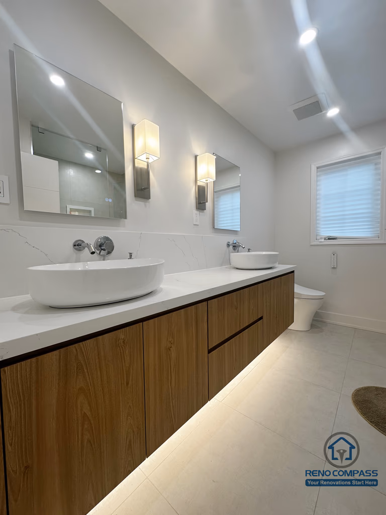 This Oakville bathroom renovation showcases a sleek floating wood vanity paired with dual vessel sinks and integrated under-cabinet lighting. The clean-lined cabinetry, quartz countertop, and wall-mounted fixtures create a balanced blend of warmth and modern minimalism, enhancing both functionality and visual openness in the space.
