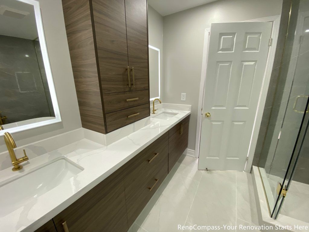This Oakville master bathroom renovation features a modern double-sink vanity with custom wood cabinetry, quartz countertop, and elegant brushed gold fixtures. The spacious layout includes integrated storage towers, LED mirrors, and a clean tile floor design that enhances both functionality and visual appeal. Designed and completed by a professional Toronto renovation company, this bathroom upgrade delivers a balance of luxury, storage efficiency, and contemporary style, creating a bright and comfortable space that adds long-term value to the home.