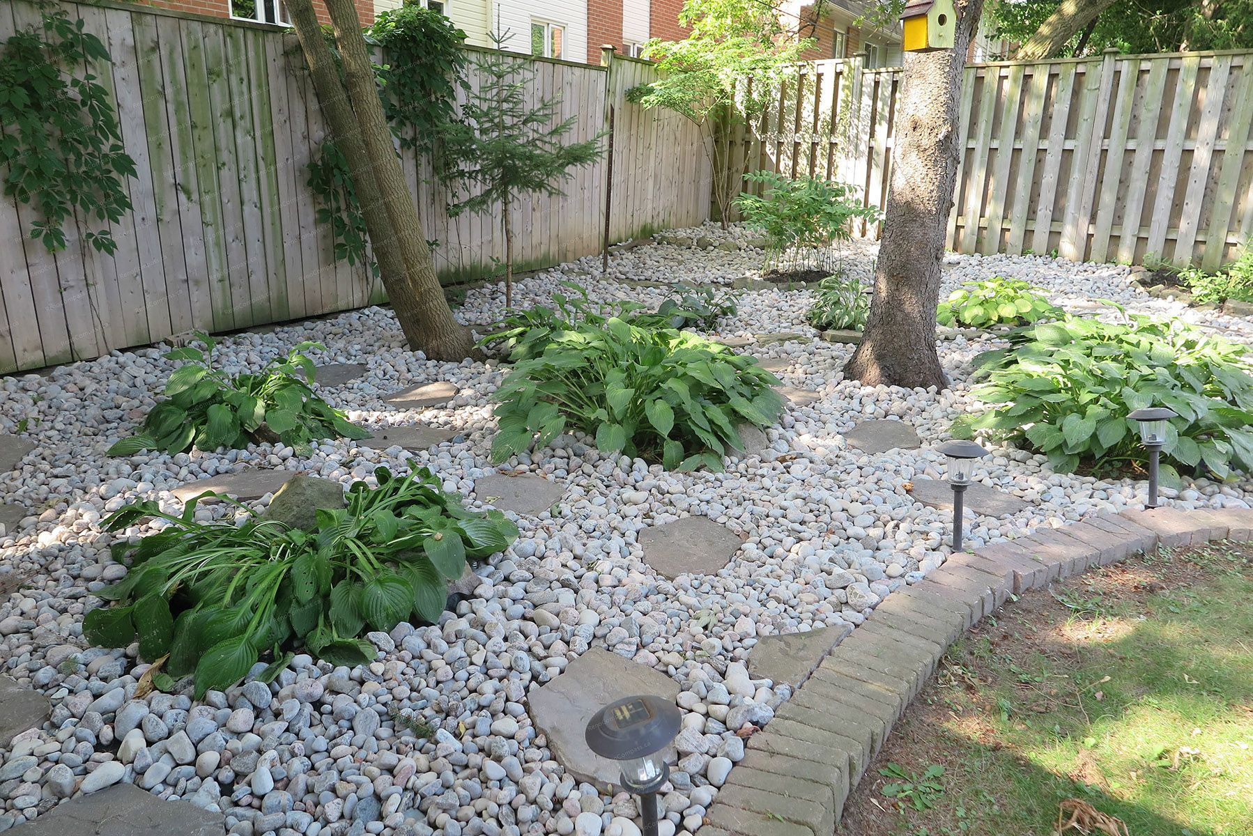 This image showcases a finished North York landscaping renovation featuring a low-maintenance decorative stone garden with natural stepping stones, mature trees, and integrated pathway lighting. The design enhances backyard drainage, visual depth, and usability while creating a calm, modern outdoor environment. Completed by a Toronto Renovation Company experienced in residential landscaping and outdoor space upgrades.