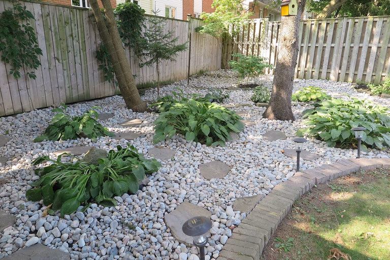 This image showcases a finished North York landscaping renovation featuring a low-maintenance decorative stone garden with natural stepping stones, mature trees, and integrated pathway lighting. The design enhances backyard drainage, visual depth, and usability while creating a calm, modern outdoor environment. Completed by a Toronto Renovation Company experienced in residential landscaping and outdoor space upgrades.