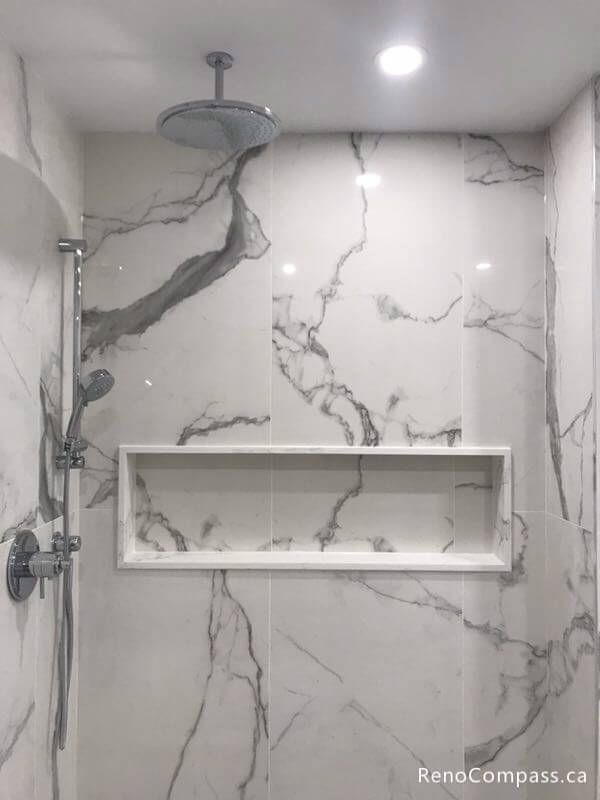 Luxury shower interior featuring a ceiling-mounted rainfall showerhead, a large built-in storage niche, and stunning marble-veined porcelain wall tiles. A premium Markham bathroom renovation detail.