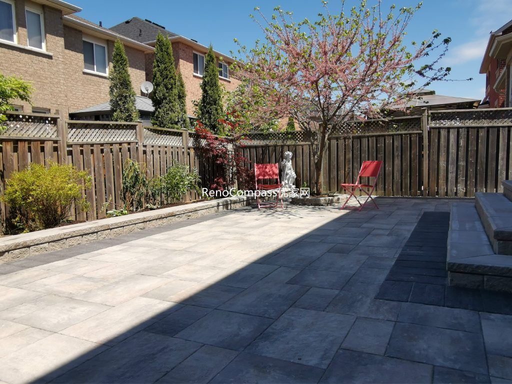 Modern Mississauga backyard patio featuring interlocking stone flooring, raised retaining wall, and landscaped garden beds, creating a functional and elegant outdoor living space.