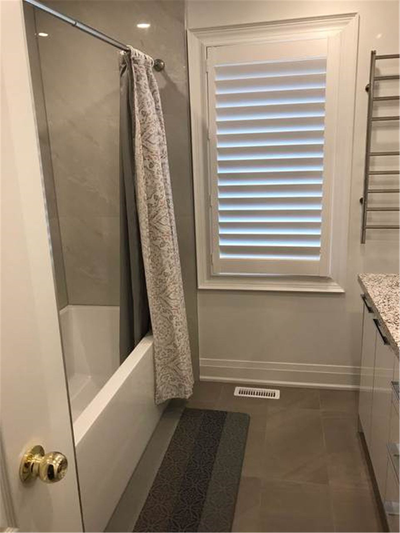 This North York bathroom renovation features a functional bathtub area with large-format tile wall finishes, a glass panel enclosure, and a window fitted with shutters for natural light and privacy. The layout emphasizes everyday comfort, moisture protection, and easy maintenance, making it ideal for family use.
