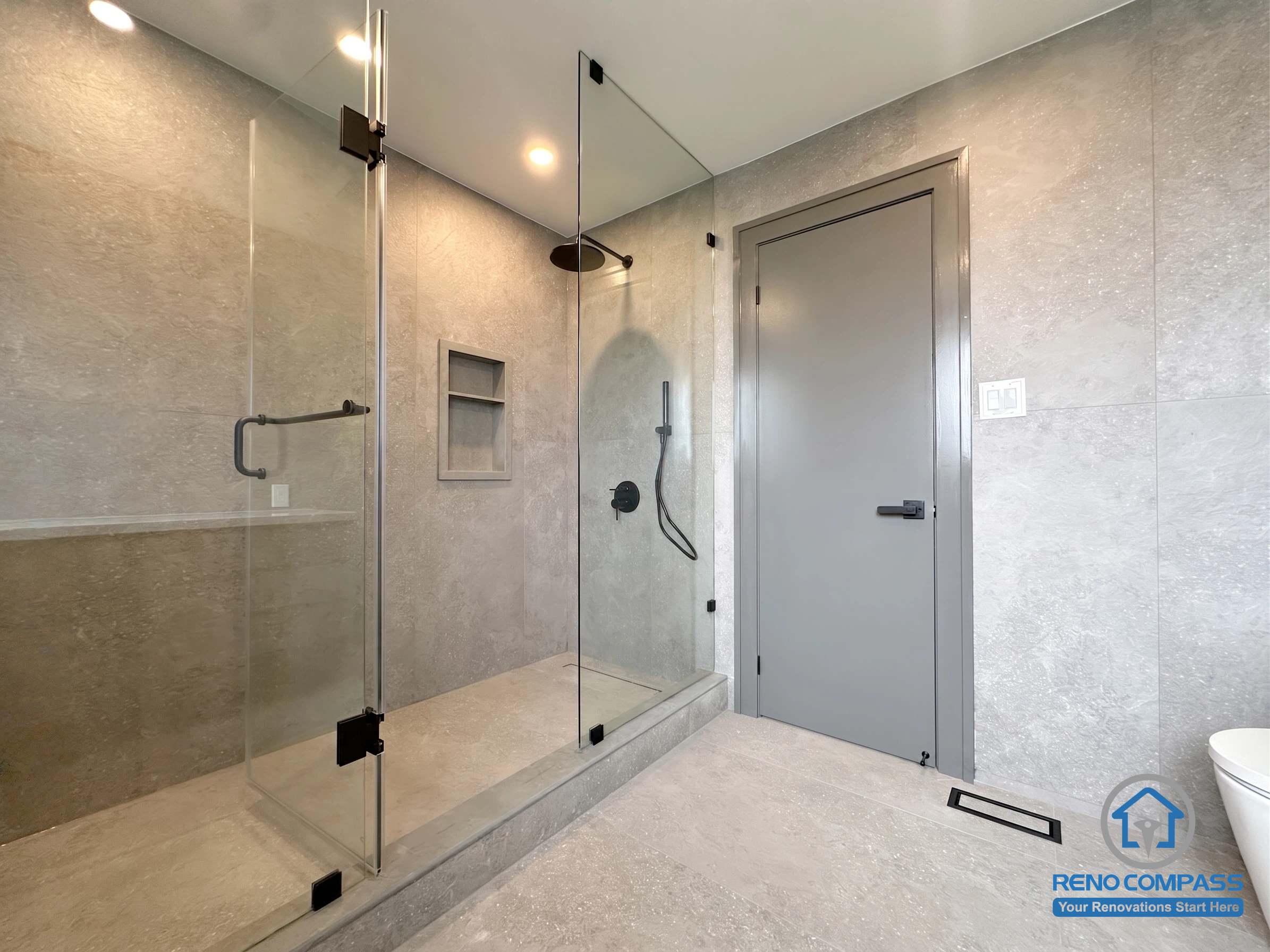 This contemporary bathroom features a frameless glass walk-in shower, recessed shower niches, matte black fixtures, and large-format porcelain tiles. Designed for both style and functionality, the spacious layout delivers a clean, spa-inspired atmosphere while offering easy maintenance and a timeless modern aesthetic. Project completed by Reno Compass, serving Markham, Toronto, Richmond Hill, Vaughan, and the Greater Toronto Area.