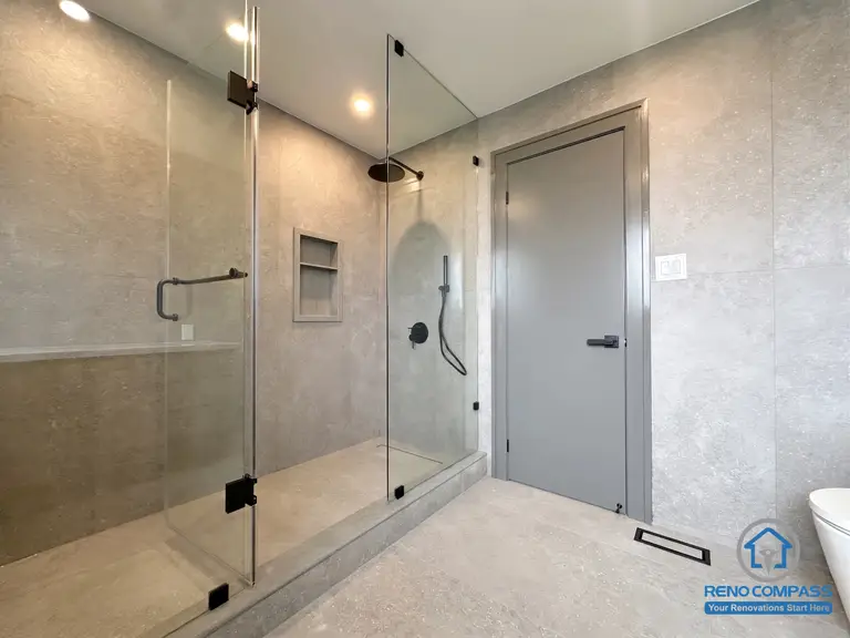 This contemporary bathroom features a frameless glass walk-in shower, recessed shower niches, matte black fixtures, and large-format porcelain tiles. Designed for both style and functionality, the spacious layout delivers a clean, spa-inspired atmosphere while offering easy maintenance and a timeless modern aesthetic. Project completed by Reno Compass, serving Markham, Toronto, Richmond Hill, Vaughan, and the Greater Toronto Area.
