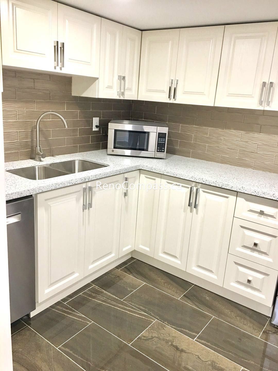 This Toronto basement renovation showcases a modern kitchenette with custom white shaker cabinets, quartz countertop, and a stylish textured backsplash. The compact layout includes a double sink, built-in microwave space, and durable tile flooring, creating a clean and functional secondary kitchen. Completed by a trusted Toronto renovation company, this basement kitchen upgrade adds convenience, value, and contemporary appeal to the home.