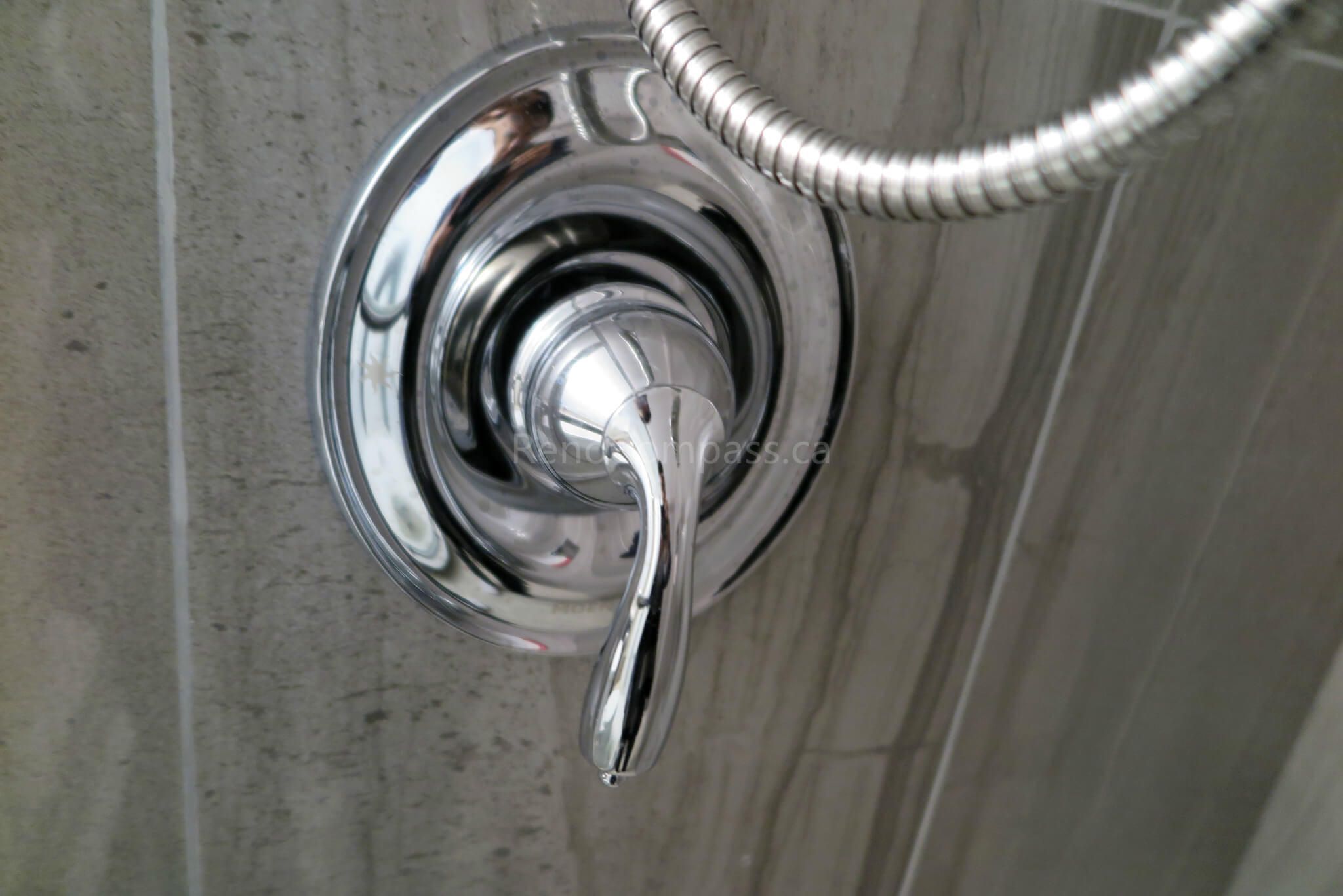 Close-up photo from a Richmond Hill basement renovation highlighting a polished chrome shower handle and control valve set against stylish grey tile. A refined bathroom detail that reflects quality craftsmanship and modern design.