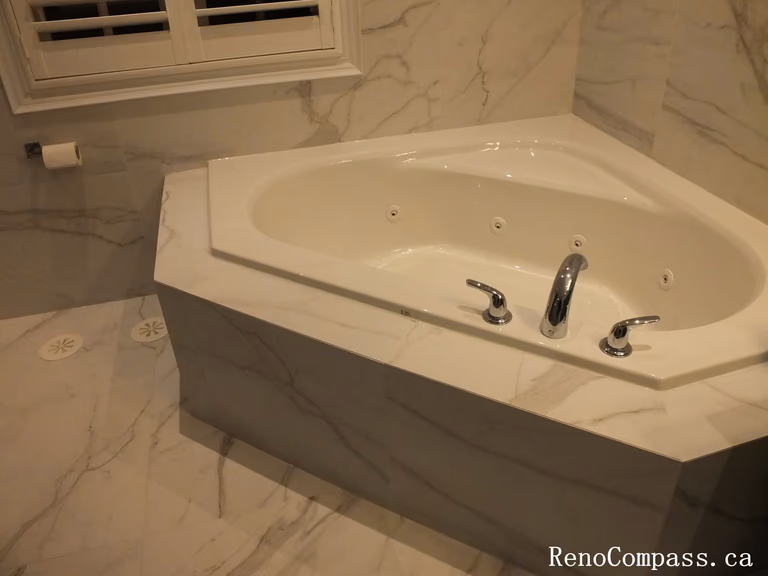 A large white corner jet tub with chrome fixtures, surrounded by custom marble-patterned porcelain tile in a Unionville home.