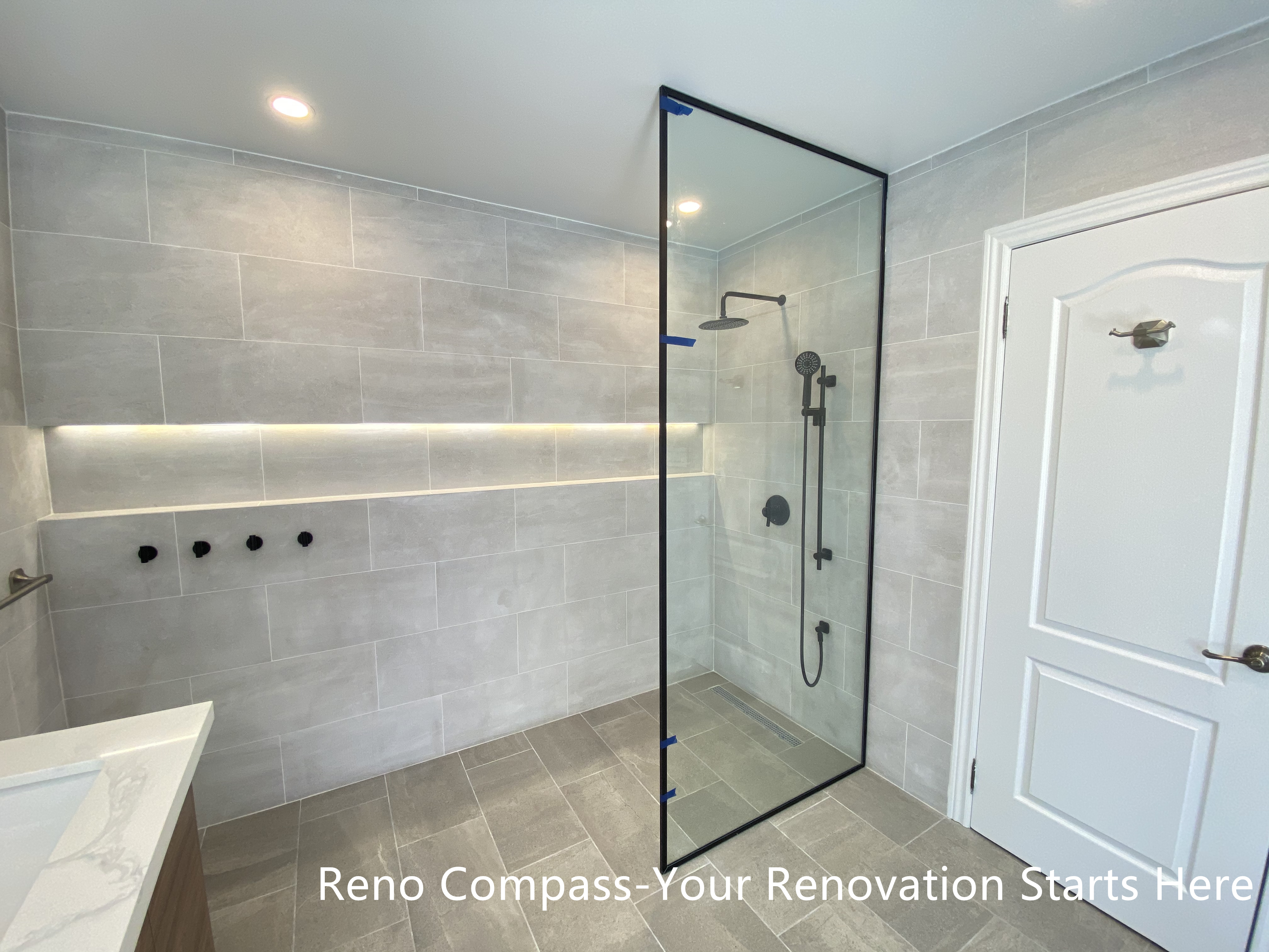 This Aurora bathroom renovation features a modern walk-in shower with a frameless glass enclosure, large-format wall tiles, and integrated niche lighting for both function and visual clarity. Matte black shower fixtures create a subtle contrast against the light tile palette, while the clean glass design maintains openness and easy circulation within the space. Recessed ceiling lighting and carefully aligned finishes contribute to a bright, refined shower environment. Designed and completed by Reno Compass, this bathroom renovation emphasizes practicality, clean detailing, and long-term usability.