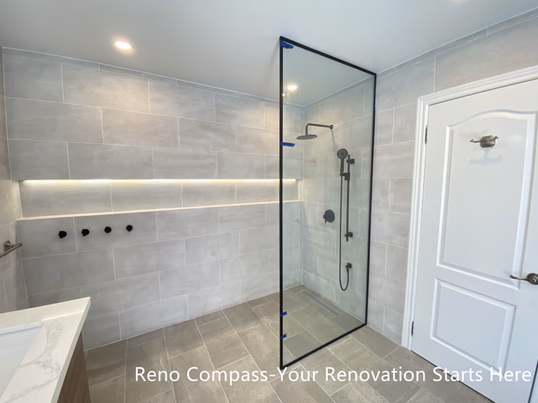 This Aurora bathroom renovation features a modern walk-in shower with a frameless glass enclosure, large-format wall tiles, and integrated niche lighting for both function and visual clarity. Matte black shower fixtures create a subtle contrast against the light tile palette, while the clean glass design maintains openness and easy circulation within the space. Recessed ceiling lighting and carefully aligned finishes contribute to a bright, refined shower environment. Designed and completed by Reno Compass, this bathroom renovation emphasizes practicality, clean detailing, and long-term usability.