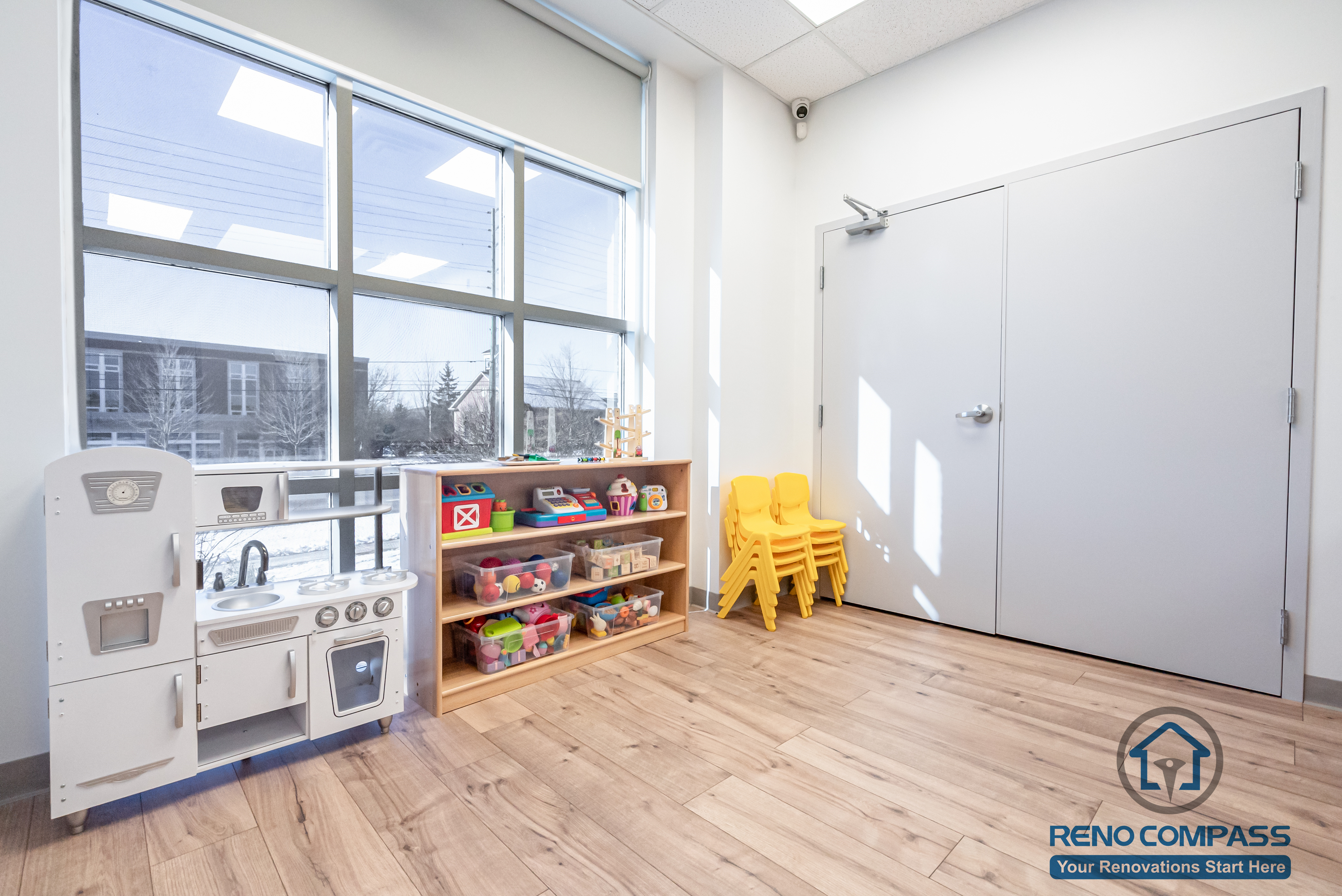 This Markham daycare renovation features a dedicated classroom activity and play corner designed to encourage creativity, independence, and safe exploration. Large windows bring in abundant natural light, creating a bright and welcoming learning environment while improving visibility for supervision. Low-height storage shelves allow children to access toys and learning materials independently, supporting early development and organization. Durable, easy-to-clean flooring ensures safety and long-term maintenance, while the open layout allows flexible use of space for different activities. Completed by a Toronto renovation company, Reno Compass Inc., this daycare interior renovation reflects a careful balance of child-centered design, safety standards, and functional planning for modern childcare facilities.