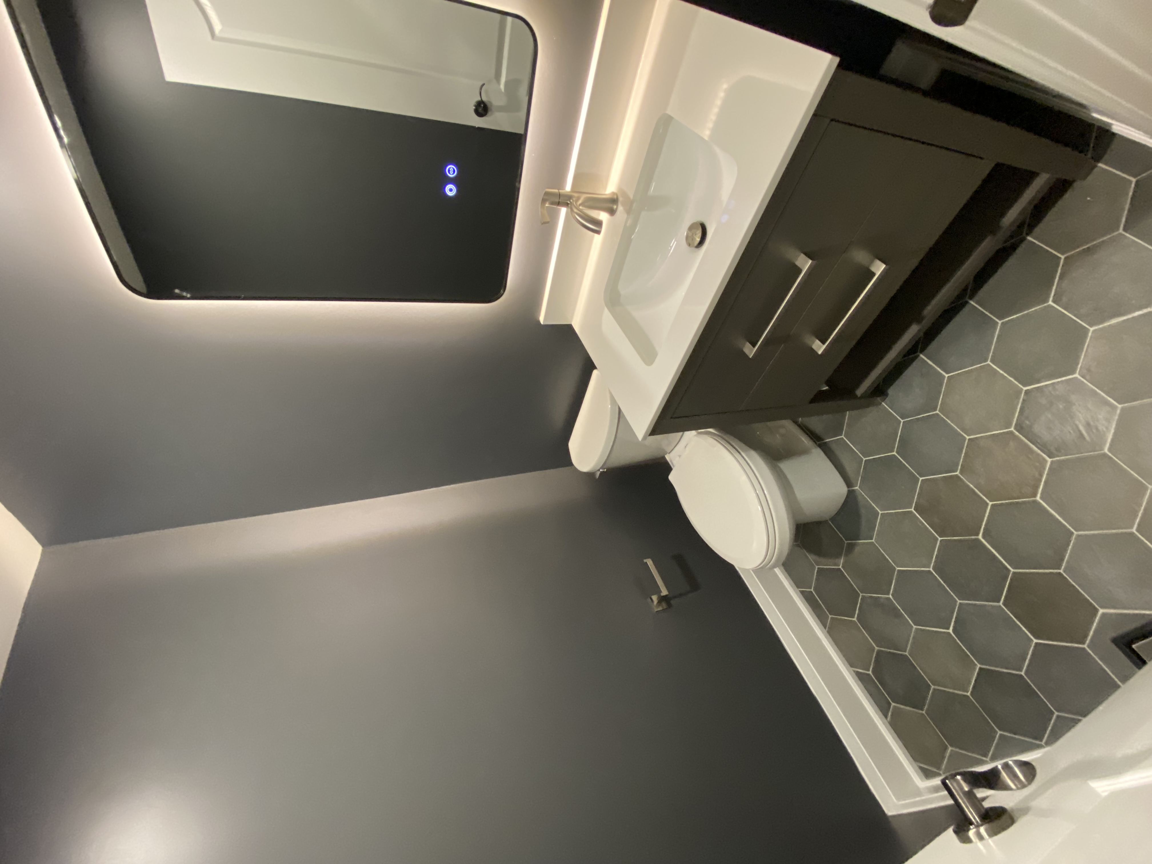 A compact powder room completed as part of a Richmond Hill interior renovation. This bathroom renovation features hexagon tile flooring, a modern vanity with integrated storage, an LED backlit mirror, and clean-lined fixtures that enhance both functionality and visual depth.