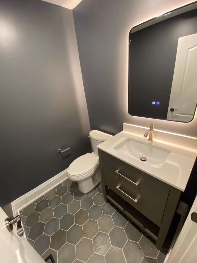 A compact powder room completed as part of a Richmond Hill interior renovation. This bathroom renovation features hexagon tile flooring, a modern vanity with integrated storage, an LED backlit mirror, and clean-lined fixtures that enhance both functionality and visual depth.