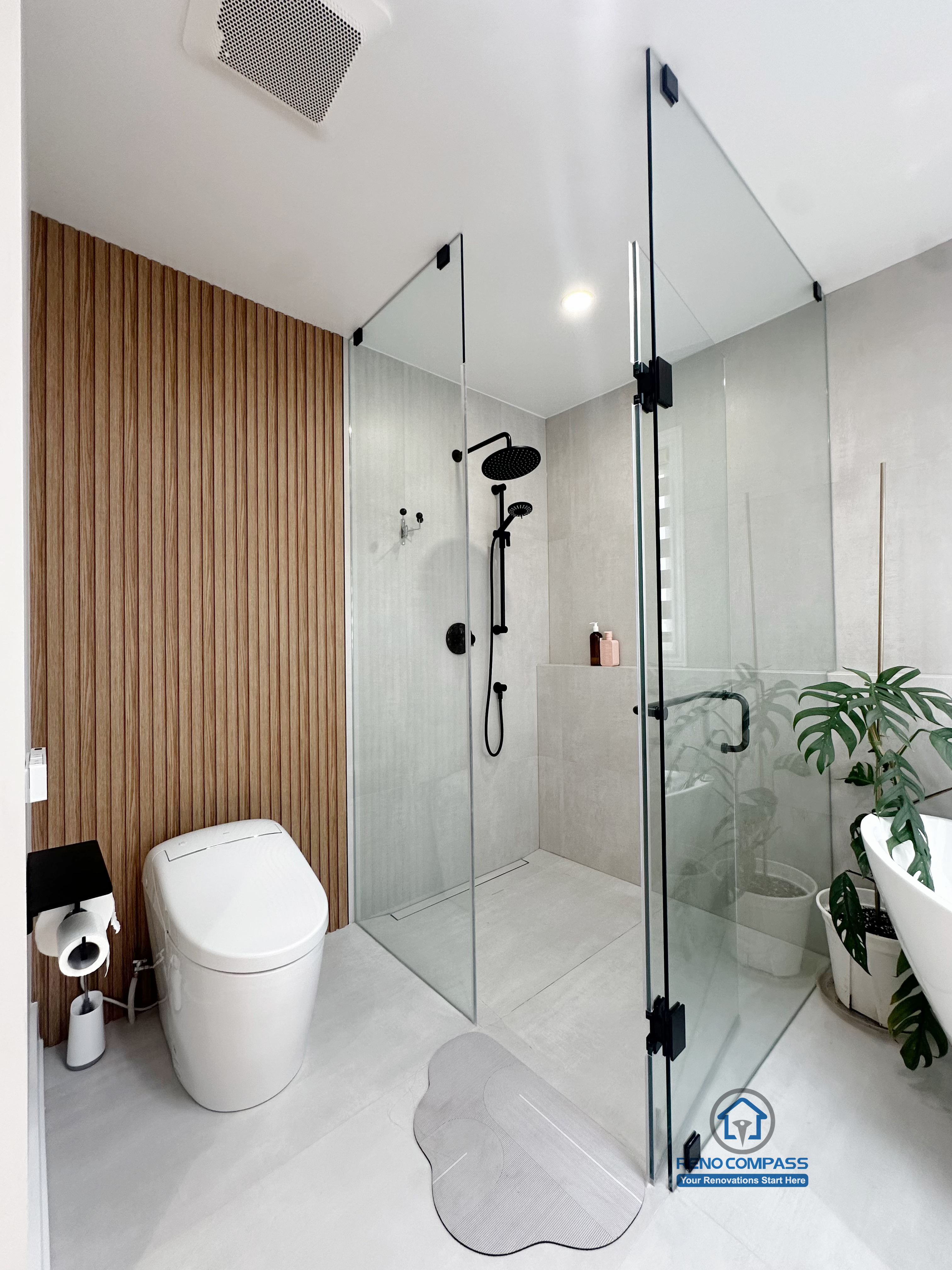A curbless bathroom renovation in Markham, Toronto by Reno Compass, featuring a walk-in glass shower, integrated toilet area, wood accent wall, and minimalist design that enhances accessibility and spatial flow.