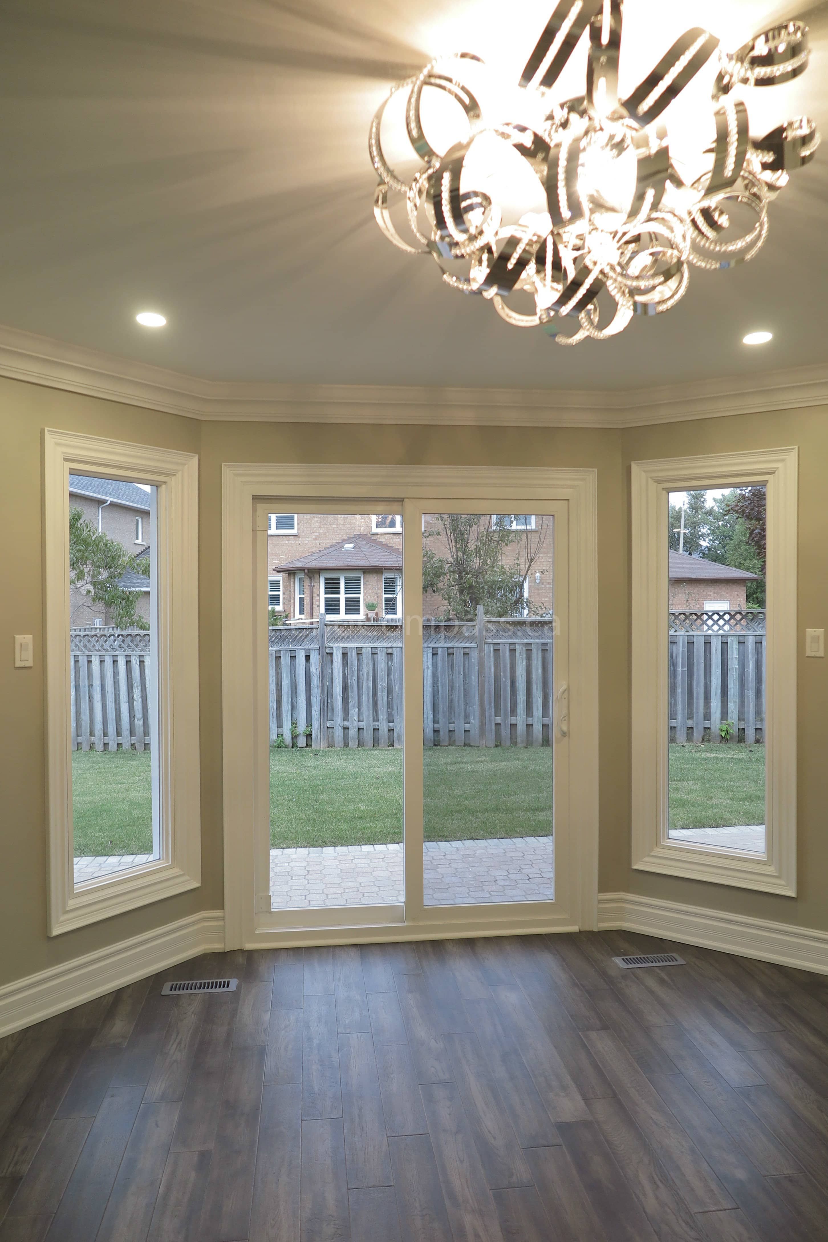 This Markham interior renovation features a bright and elegant space with large custom windows and a central sliding patio door that brings in abundant natural light and backyard views. The room is finished with detailed crown molding, classic trim work, and newly installed dark hardwood flooring, creating a warm and refined atmosphere. Completed by Reno Compass, a trusted renovation contractor specializing in interior renovations and custom finishing services across Markham and the Greater Toronto Area.