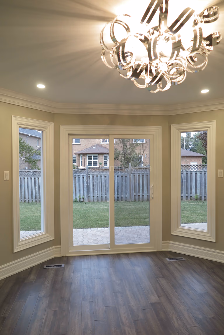This Markham interior renovation features a bright and elegant space with large custom windows and a central sliding patio door that brings in abundant natural light and backyard views. The room is finished with detailed crown molding, classic trim work, and newly installed dark hardwood flooring, creating a warm and refined atmosphere. Completed by Reno Compass, a trusted renovation contractor specializing in interior renovations and custom finishing services across Markham and the Greater Toronto Area.