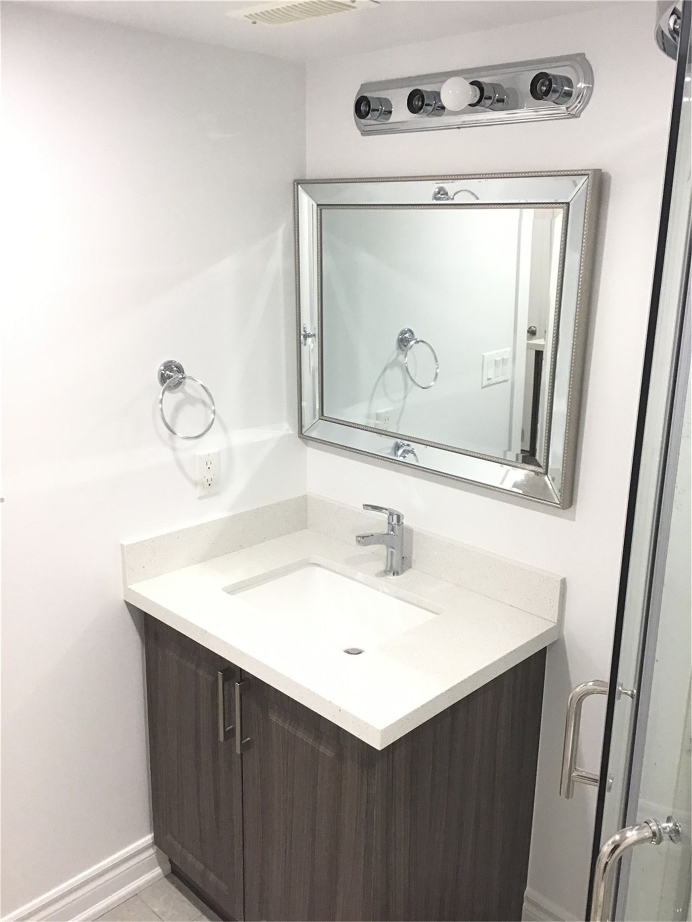 This Mississauga basement bathroom renovation features a modern vanity with wood-grain cabinetry, a sleek white countertop sink, and a framed mirror with updated lighting. Completed by a professional Toronto Renovation Company, the design focuses on clean lines, efficient space use, and durable finishes—creating a bright, functional bathroom ideal for a finished basement or secondary living suite.