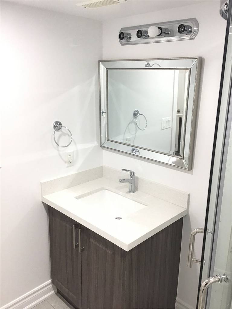 This Mississauga basement bathroom renovation features a modern vanity with wood-grain cabinetry, a sleek white countertop sink, and a framed mirror with updated lighting. Completed by a professional Toronto Renovation Company, the design focuses on clean lines, efficient space use, and durable finishes—creating a bright, functional bathroom ideal for a finished basement or secondary living suite.