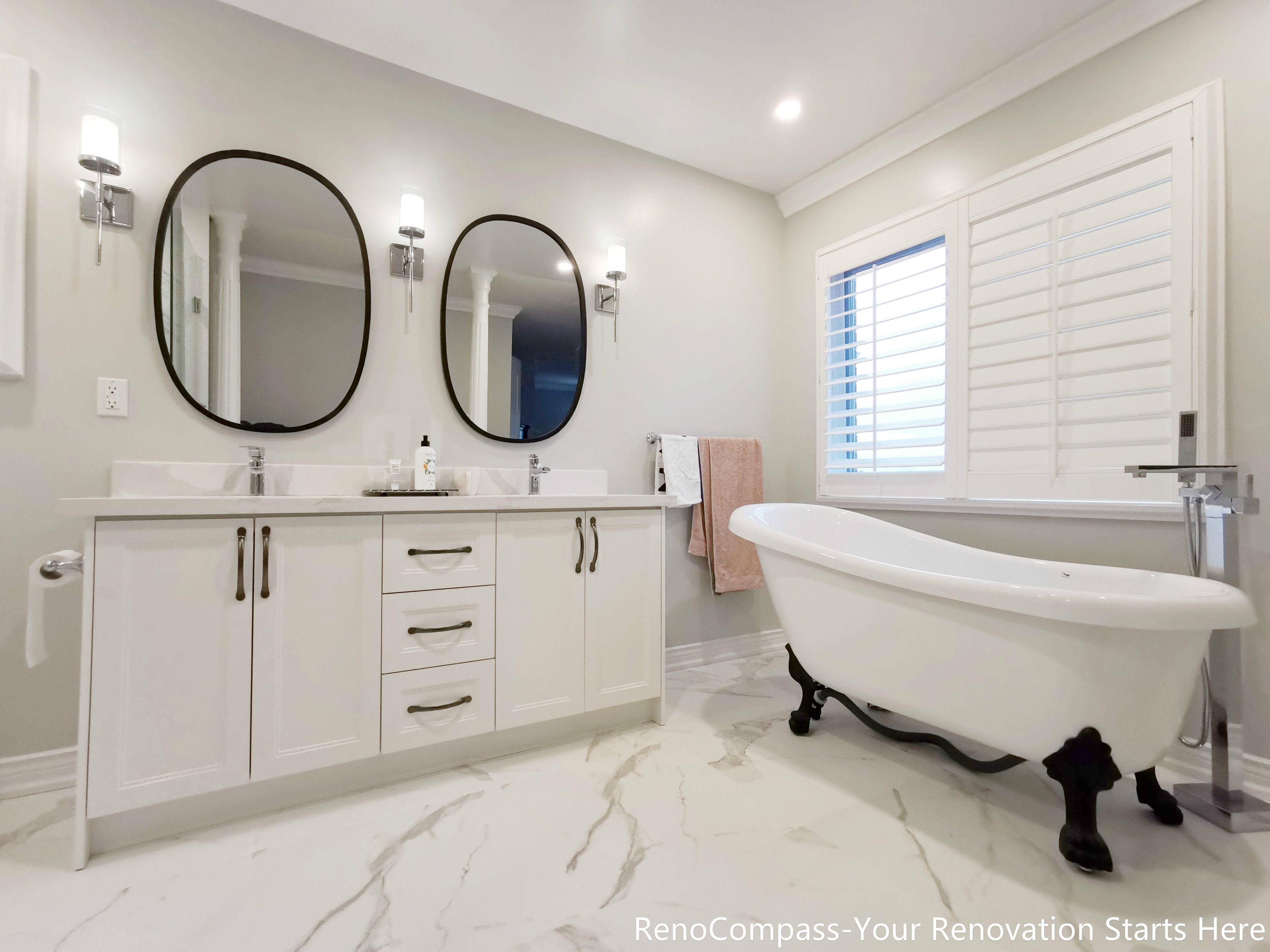This image features a double vanity design from an Oakville bathroom renovation, highlighting two oval mirrors positioned symmetrically above custom cabinetry. The mirror frames and cabinet hardware share the same finish, creating a cohesive and refined visual rhythm. Paired with marble flooring and soft wall lighting, the space feels balanced, elegant, and highly functional, offering a well-considered layout for shared daily use while maintaining a calm, upscale atmosphere.