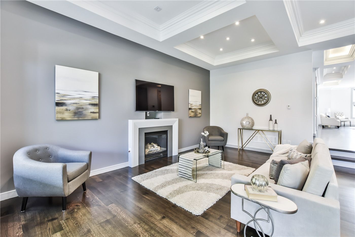 This Toronto interior design pre-sale staging showcases a modern living room with elegant coffered ceilings, recessed lighting, and rich hardwood flooring. The sleek fireplace feature wall with mounted TV, neutral-tone seating, and contemporary décor create a bright and refined atmosphere.