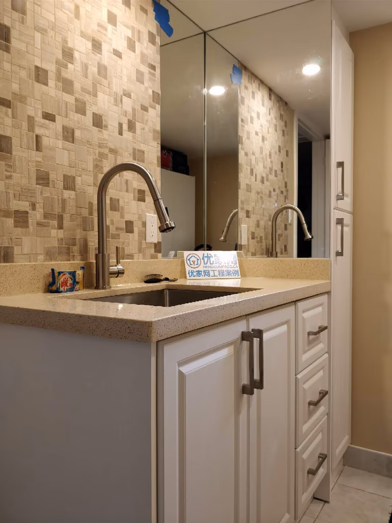 Stylish basement wet bar area completed as part of a Scarborough interior renovation. The design features custom white cabinetry, quartz countertop, modern pull-down faucet, mosaic tile backsplash, and a large wall mirror to enhance light and depth, creating a functional and elegant entertainment space for the home.