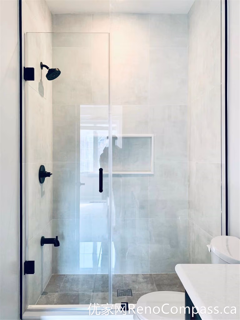 This walk-in shower from a Markham home renovation features a frameless glass enclosure, matte black fixtures, and a built-in wall niche for convenient storage. The neutral tile design and clean layout provide a modern, low-maintenance solution that balances style and everyday functionality.