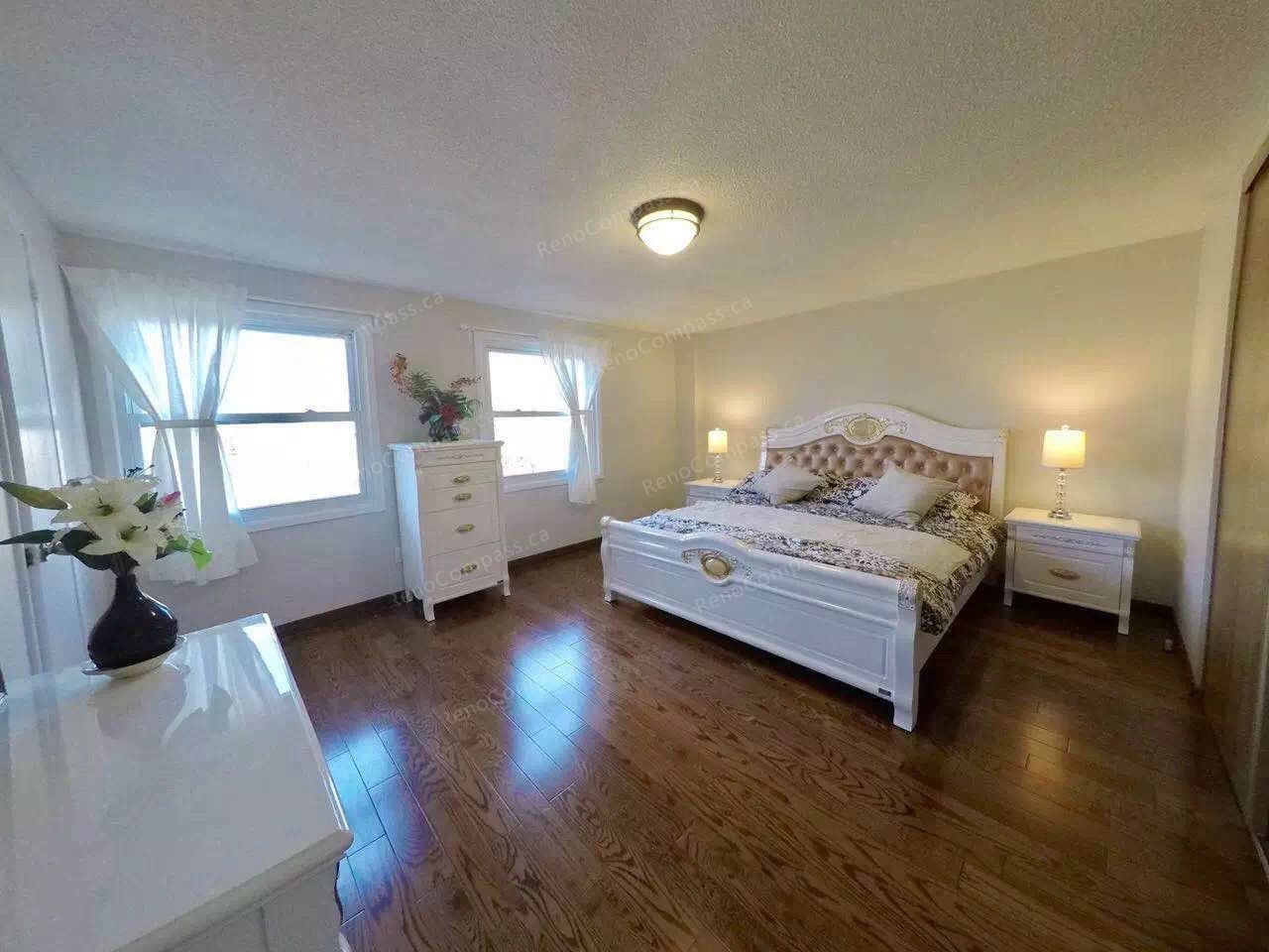 After renovation view of a spacious and bright bedroom in a Scarborough home featuring refreshed hardwood flooring, updated lighting, and a clean modern layout. Large windows bring in natural light while the upgraded interior creates a warm and comfortable living environment. Completed by a trusted Toronto renovation company, this bedroom renovation enhances both functionality and aesthetic appeal for everyday living.
