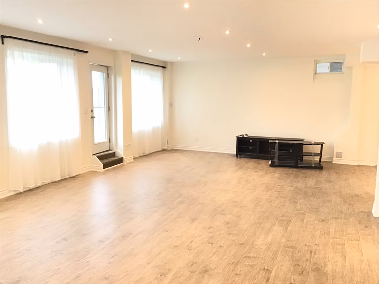This Aurora basement renovation showcases a bright and spacious open-concept living area featuring wide plank flooring, recessed pot lights, and large windows for natural light. The clean layout and neutral palette create a versatile space ideal for a family room, entertainment area, or home office.