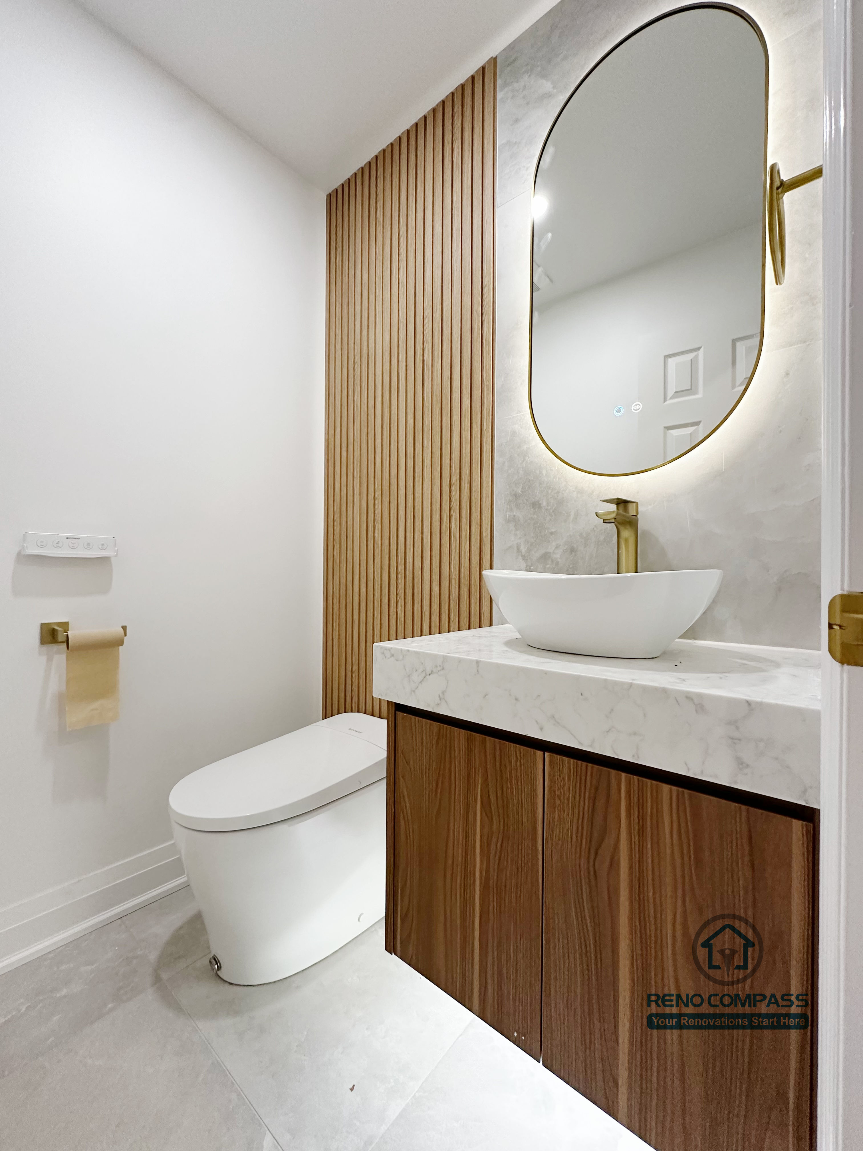 Bathroom renovation in Markham featuring a custom wood vanity with quartz countertop, vessel sink, brass fixtures, and a rounded backlit mirror. Vertical wood paneling and minimalist finishes create a warm, modern powder room with clean proportions and refined detailing.