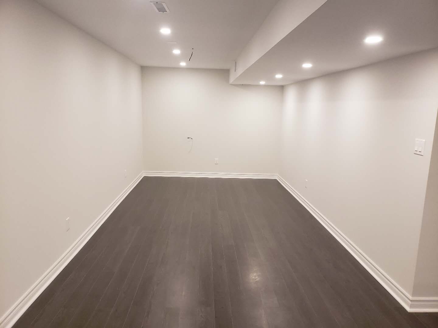 This finished basement renovation in Markham features a clean and spacious open-concept layout designed for flexible living. The area is upgraded with durable dark flooring, smooth neutral walls, and modern recessed pot lights that provide balanced illumination throughout the space. The streamlined ceiling design and updated baseboards enhance the overall contemporary look while maximizing usable square footage. This professionally renovated basement offers a versatile environment ideal for a recreation room, home office, or entertainment space, reflecting high-quality craftsmanship and practical design commonly seen in modern Markham basement renovations.