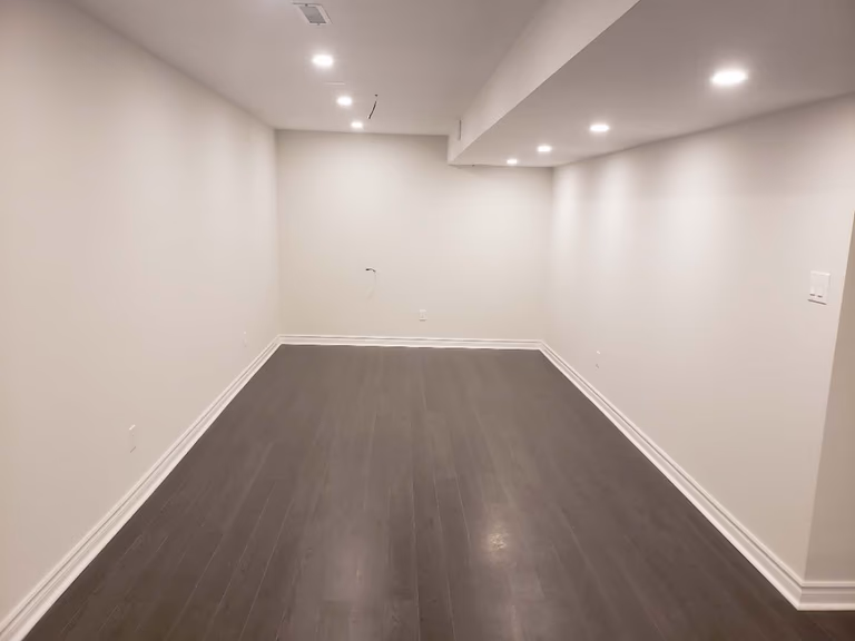 This finished basement renovation in Markham features a clean and spacious open-concept layout designed for flexible living. The area is upgraded with durable dark flooring, smooth neutral walls, and modern recessed pot lights that provide balanced illumination throughout the space. The streamlined ceiling design and updated baseboards enhance the overall contemporary look while maximizing usable square footage. This professionally renovated basement offers a versatile environment ideal for a recreation room, home office, or entertainment space, reflecting high-quality craftsmanship and practical design commonly seen in modern Markham basement renovations.
