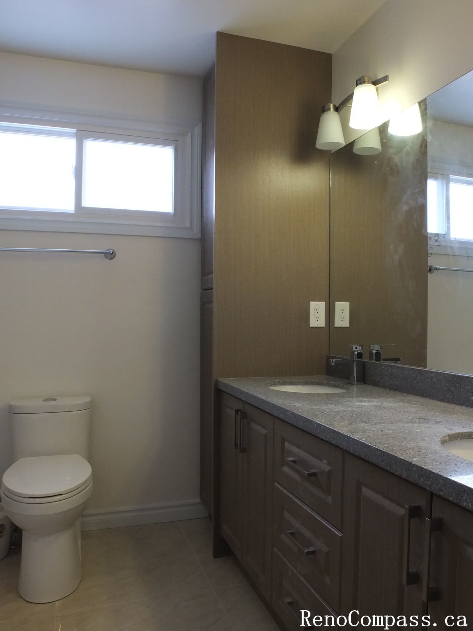 Bathroom renovation in North York showcasing a wood-tone vanity with integrated storage, quartz countertop, wall-mounted mirror, and modern lighting. This interior renovation highlights practical layout planning, neutral finishes, and long-term durability for Toronto residential homes.