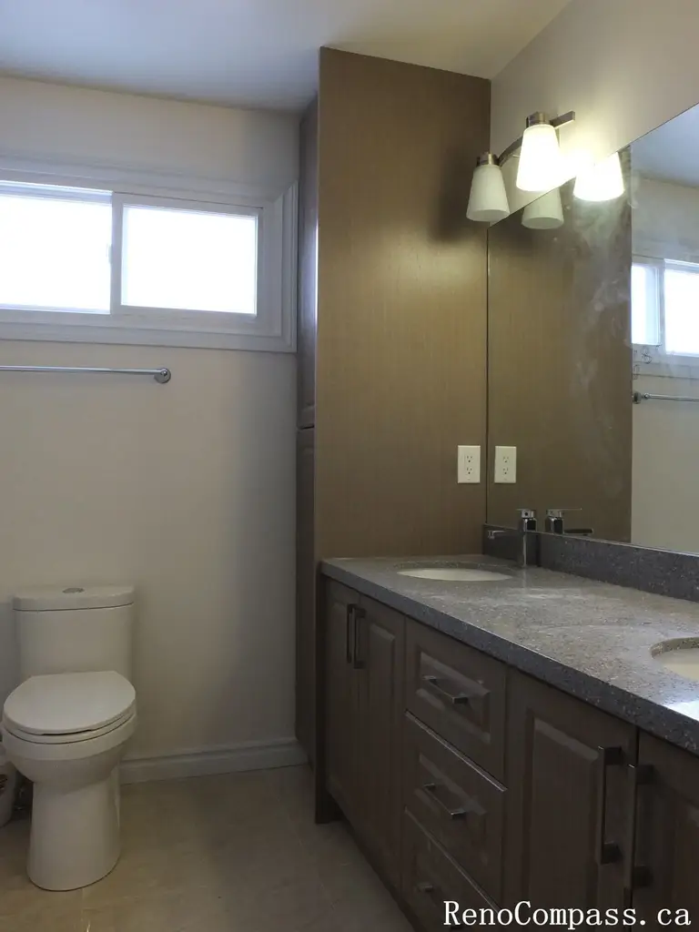 Bathroom renovation in North York showcasing a wood-tone vanity with integrated storage, quartz countertop, wall-mounted mirror, and modern lighting. This interior renovation highlights practical layout planning, neutral finishes, and long-term durability for Toronto residential homes.