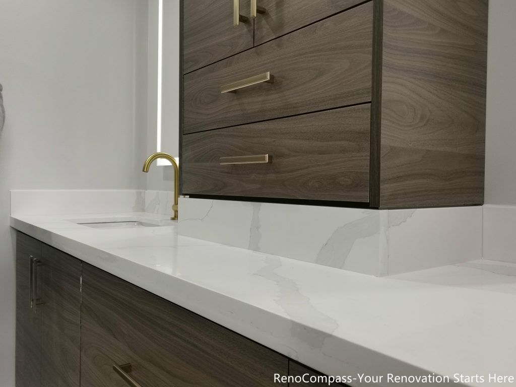 This Oakville master bathroom renovation features a sleek quartz countertop paired with custom wood vanity cabinetry and brushed gold fixtures for a refined modern look. The clean countertop edges, undermount sink, and matching storage drawers create a functional and elegant vanity space. Designed and completed by a professional Toronto renovation company, this bathroom upgrade focuses on durability, storage efficiency, and timeless contemporary design, enhancing both daily usability and overall home value.