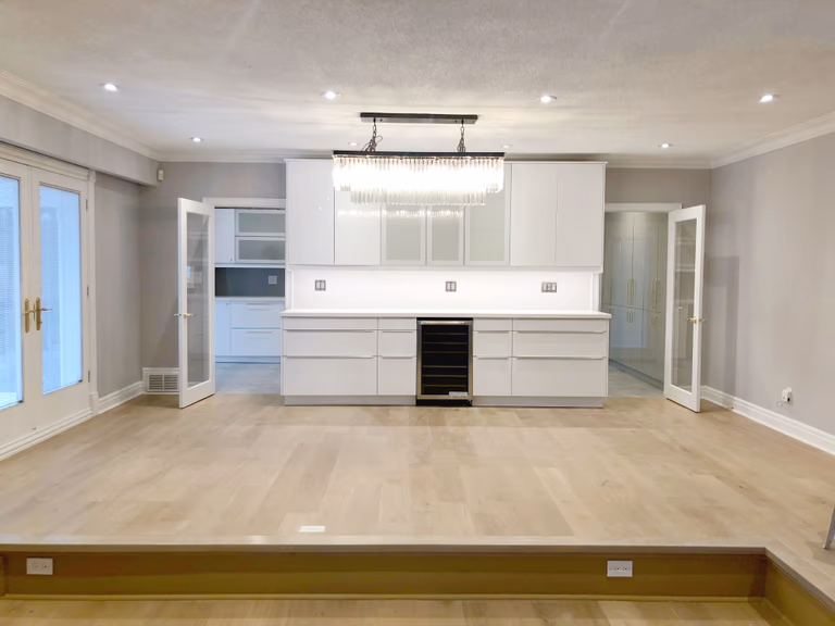 This Etobicoke interior renovation showcases a spacious open-concept living area with custom-built cabinetry, modern lighting, and upgraded flooring for a clean and refined look. The feature wall with integrated storage and wine cooler enhances both functionality and visual balance, while recessed lighting and large windows improve overall brightness. Designed and completed by Reno Compass Inc., this renovation focuses on modern comfort, practical layout planning, and timeless finishes that elevate everyday living.