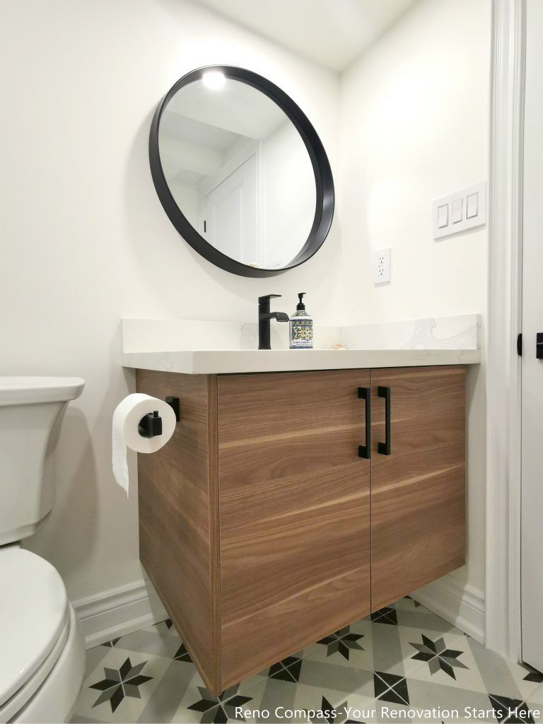 This image highlights a detailed view of a renovated basement bathroom vanity in Vaughan, featuring a modern wood-tone cabinet with integrated storage and a clean quartz countertop. A round wall-mounted mirror and matte black fixtures add a contemporary touch while maintaining a simple and functional layout. Patterned tile flooring enhances visual interest and durability, making the space easy to maintain for everyday basement use. This bathroom renovation detail reflects careful material selection, precise installation, and quality craftsmanship delivered by a professional Toronto renovation company.