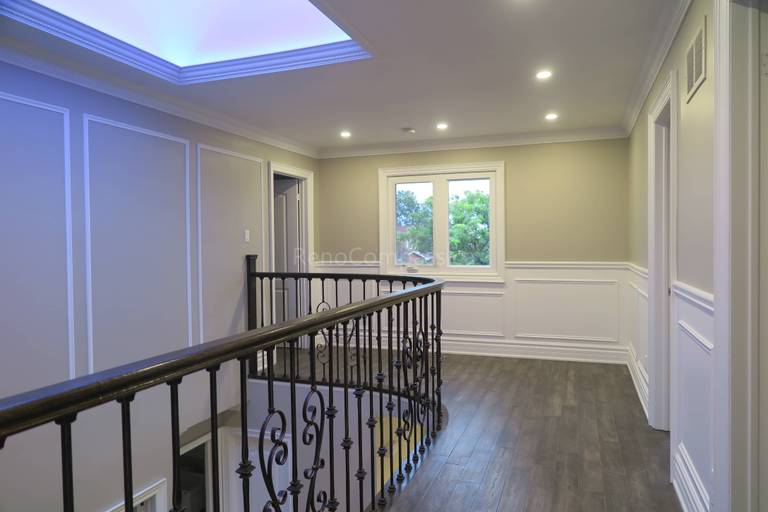 This Markham interior renovation showcases an elegant upper hallway and staircase area featuring custom wrought iron railings, detailed wall panel molding, and modern hardwood flooring. The space is enhanced by recessed lighting and a contemporary tray ceiling with soft ambient illumination, creating a bright and refined transition between levels. Completed by Reno Compass, a trusted renovation contractor specializing in custom interior finishing and full home renovations across Markham and the Greater Toronto Area.