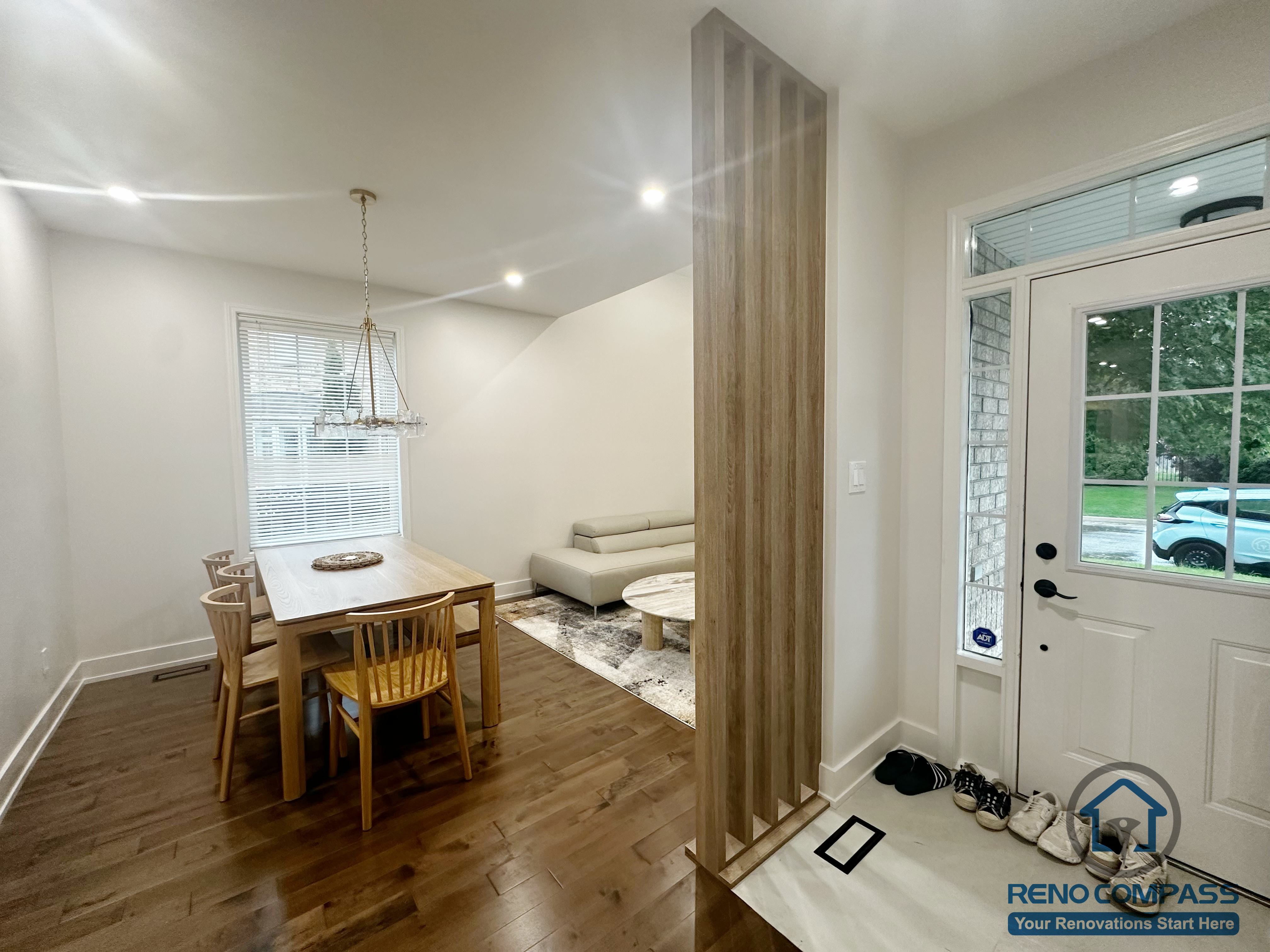 This Oakville interior renovation highlights an open-concept dining area seamlessly connected to the home’s entryway. A vertical wood slat divider subtly defines the space without blocking natural light or sightlines, creating a sense of separation while maintaining openness. Warm hardwood flooring extends throughout the dining area, complemented by clean wall finishes and recessed lighting. The layout balances everyday dining, circulation, and entry storage needs, resulting in a functional and visually cohesive transition between shared living spaces in a modern home.
