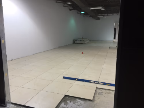 该图片展示一万平方尺娱乐室内中心在地面施工阶段的实拍画面，由专业多伦多装修公司负责整体商业空间翻新工程。现场正在进行大面积地砖铺设与水平校准作业，确保地面平整度与耐用性符合商业使用标准。项目涵盖地面找平、防水处理及高强度瓷砖安装，为后续娱乐区域布局与设备安装提供稳固基础。通过规范化施工流程与精细化质量把控，全面提升大型商业空间的整体品质与使用体验。