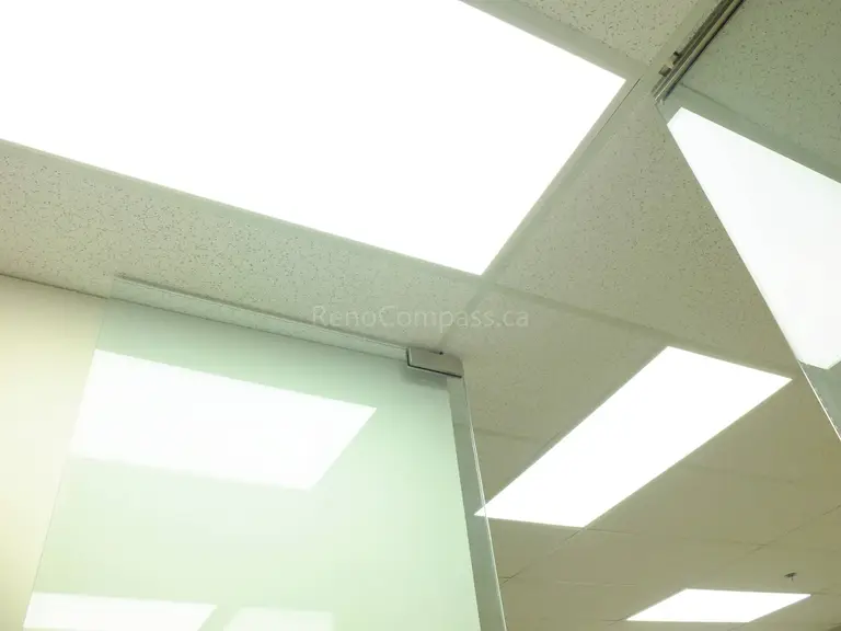 This image showcases bright LED panel lights installed in a modern North York office ceiling. The energy-efficient lighting design enhances the professional atmosphere, providing uniform illumination across the workspace while complementing the suspended acoustic ceiling system and glass office partitions.
